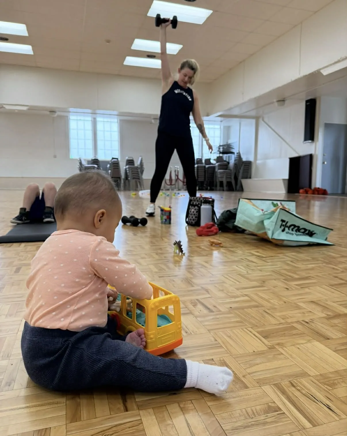 Baby playing with toys in the foreground while mom works out during class