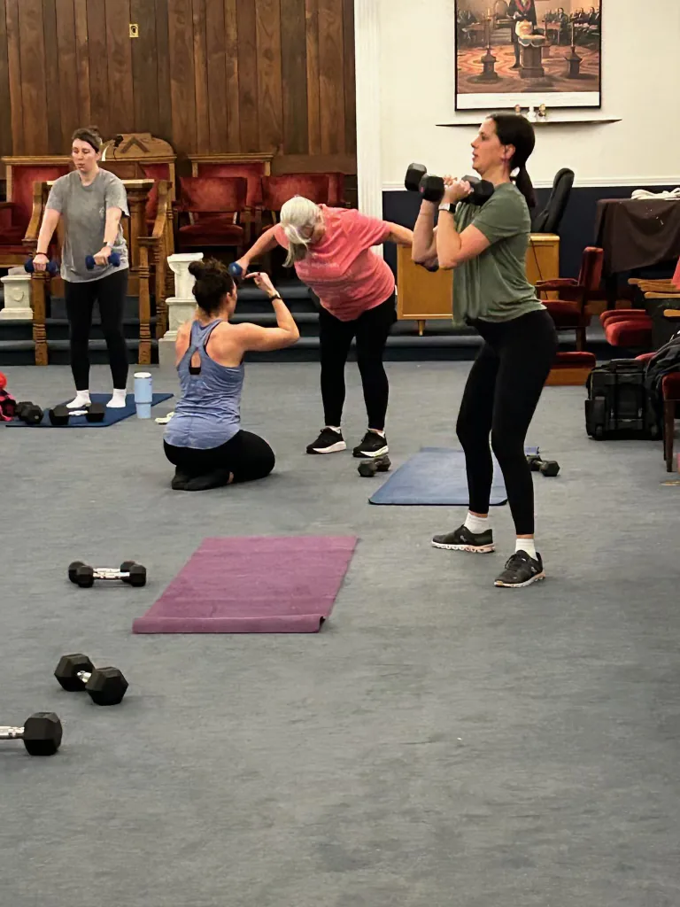 Coach Brittany crouched beside a member, adjusting her form mid-set