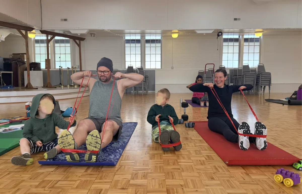 Husband and wife doing banded face pulls on mats while their kids play alongside them