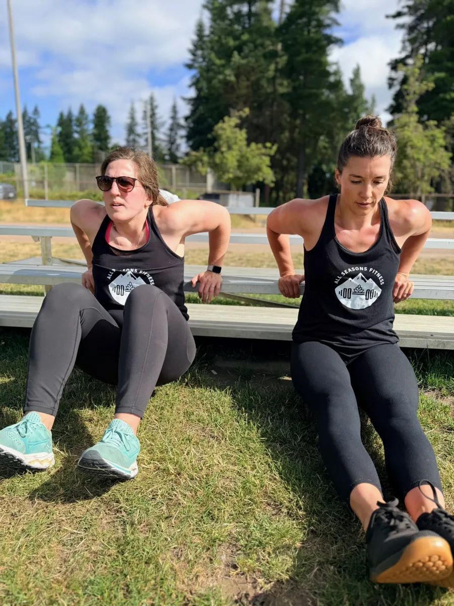 Coach Brittany and member doing tricep dips in All Seasons Fitness branded tanks